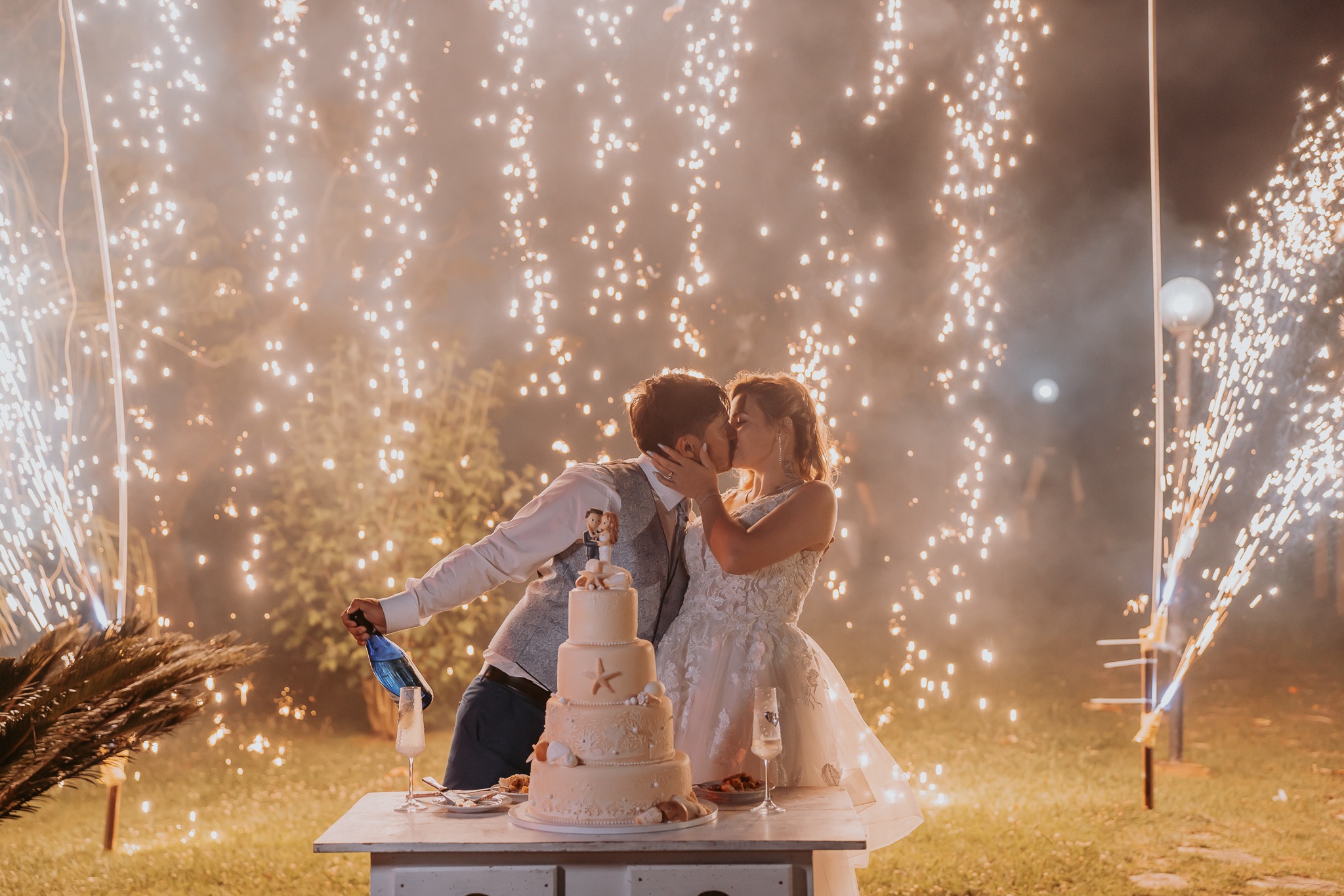 Casal a cortar o bolo com fogo de artifício no casamento